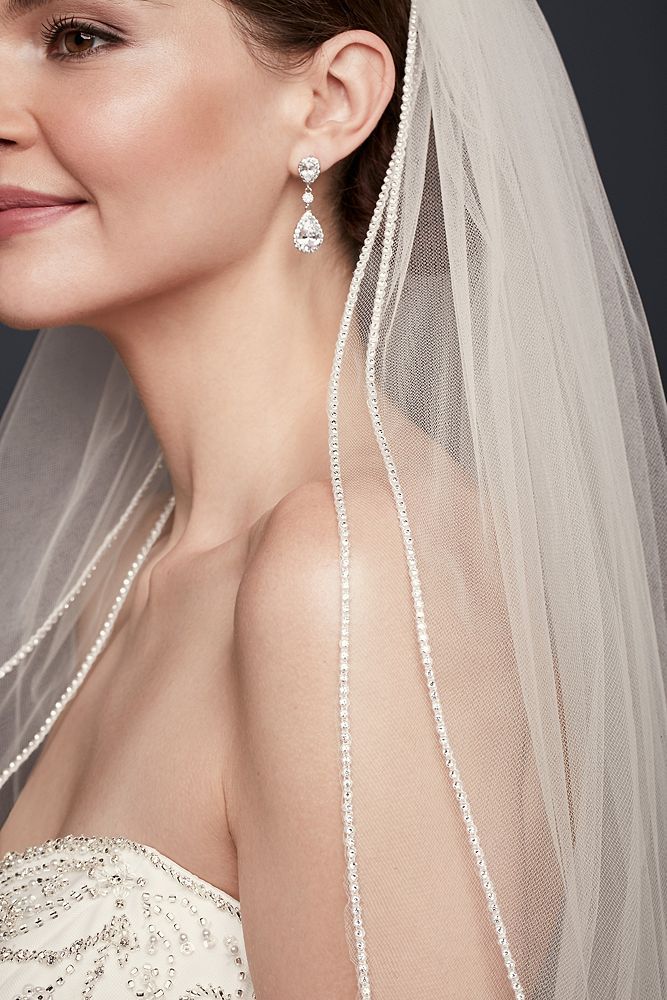 a woman in a wedding dress wearing a veil with pearls on the head and shoulder