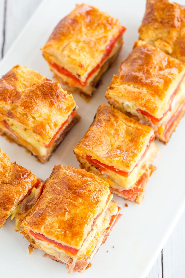 several square sandwiches on a white platter with cheese and tomato sauce, cut into squares