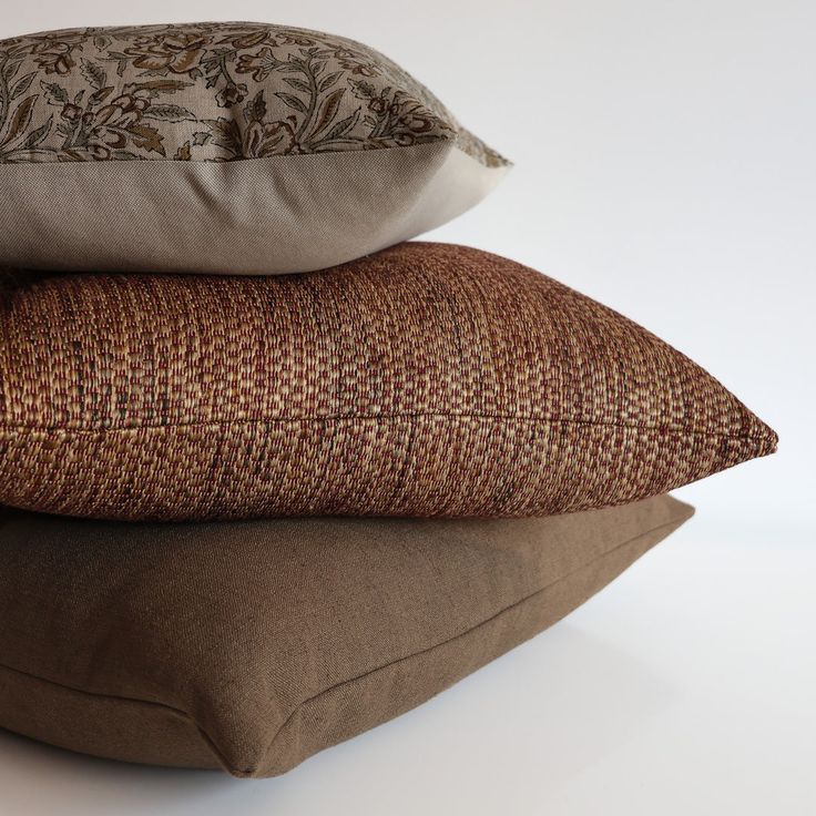 three pillows stacked on top of each other in front of a white background and one is brown