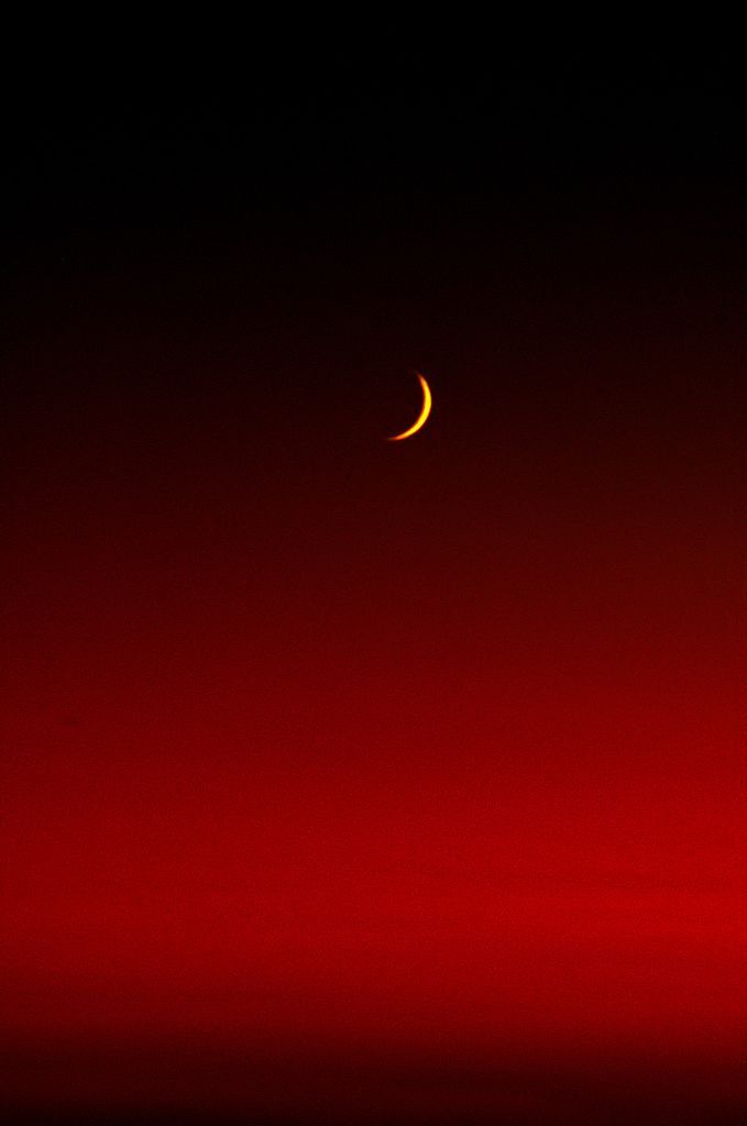 the moon is seen in the dark red sky