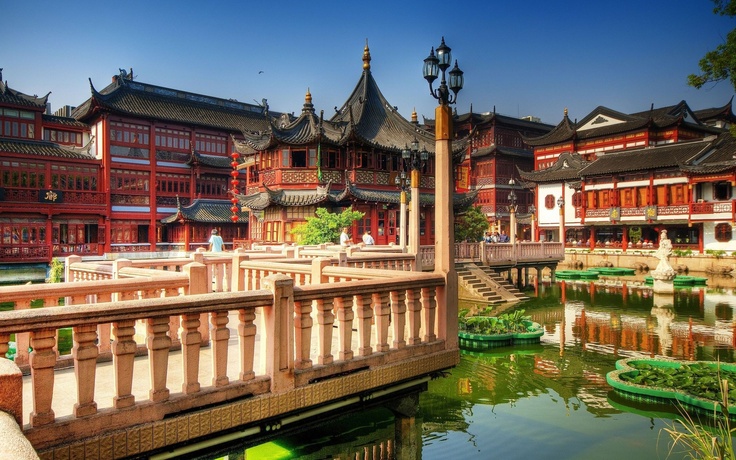 an old chinese city with many buildings and green plants in the water's edge