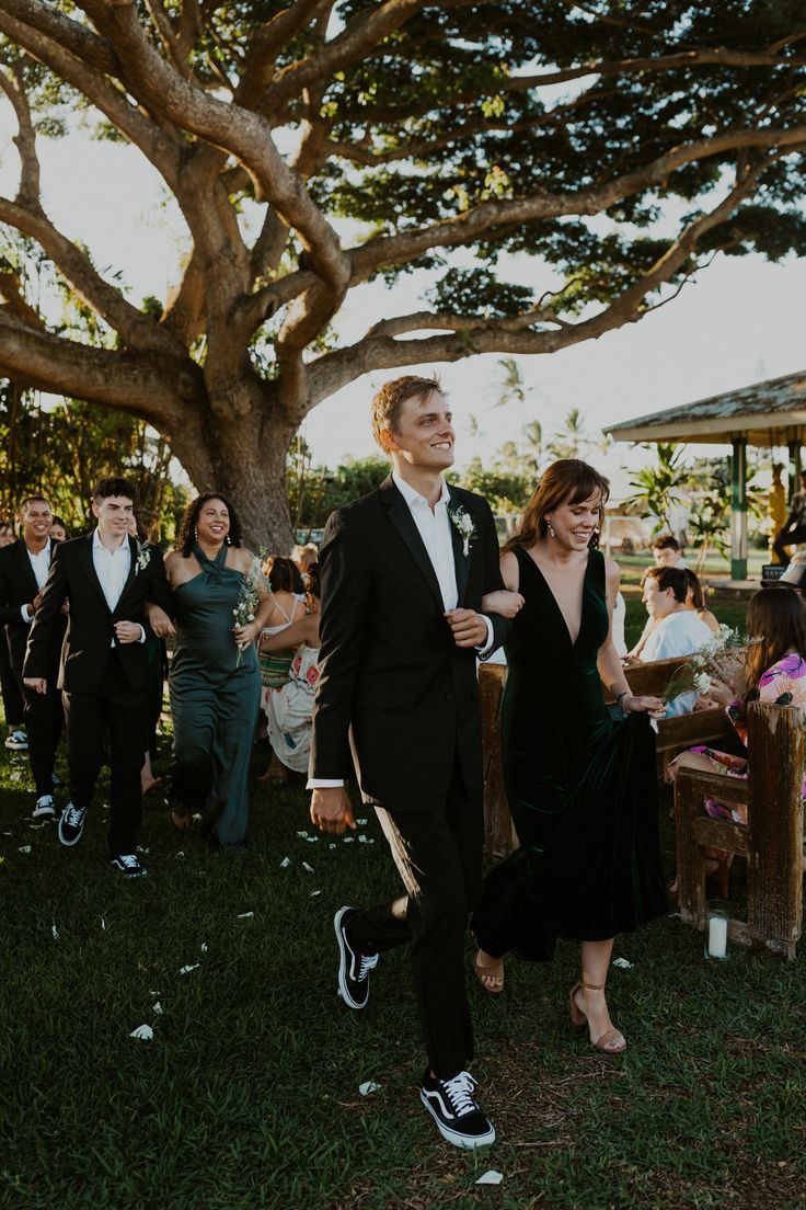 a man and woman in formal wear walking down the aisle at an outdoor wedding ceremony