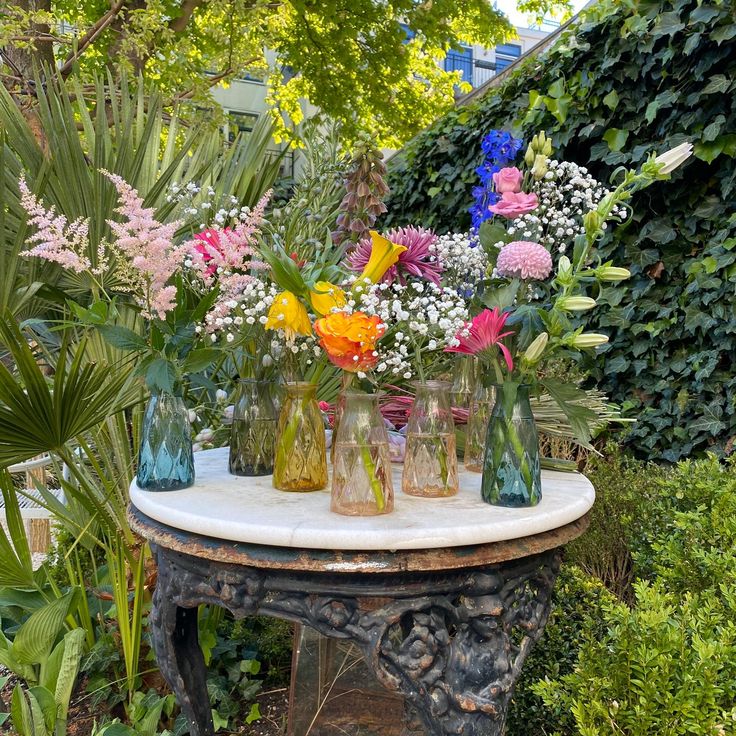 a table with vases filled with flowers on top of it in front of some bushes