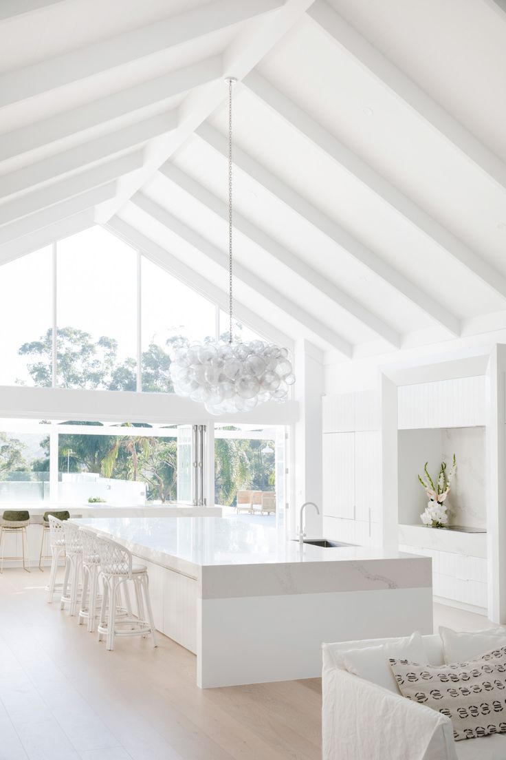 a white kitchen with an island in the middle and lots of windows on both sides