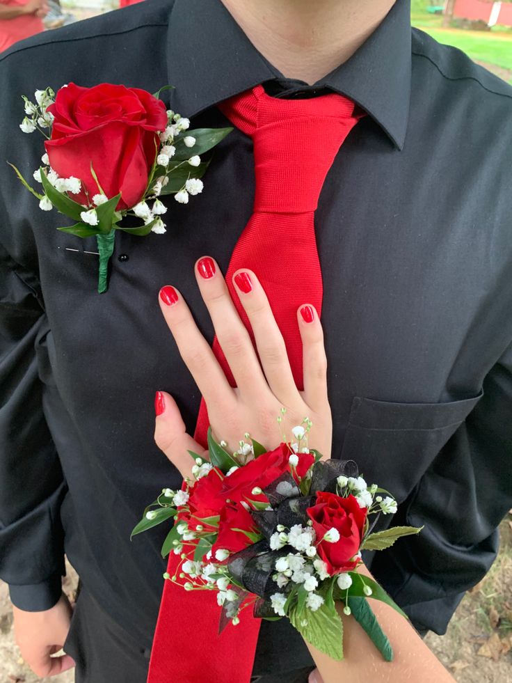 a man wearing a red tie and matching boutonniere is holding a bouquet of flowers