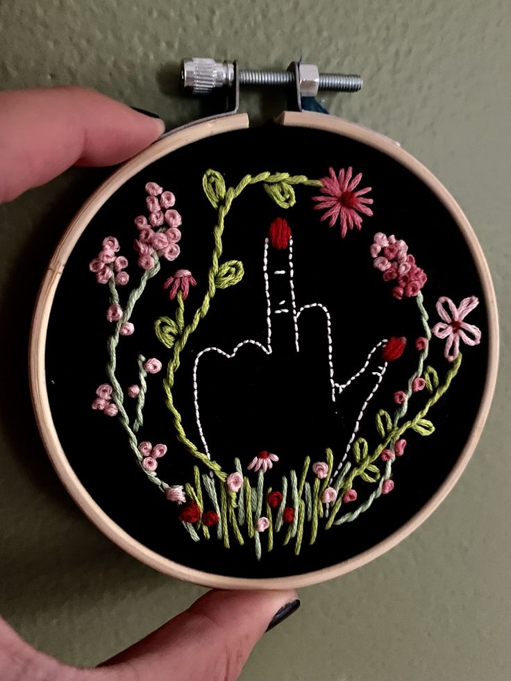 someone is holding up a hand embroidered on a black background with pink and green flowers