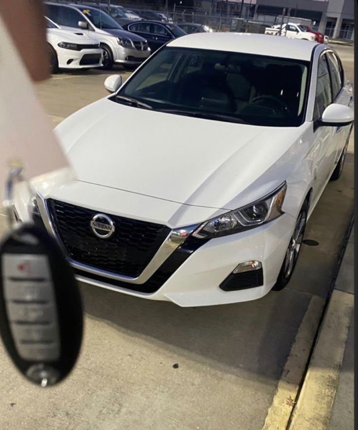 a white car parked in a parking lot next to a person holding a cell phone