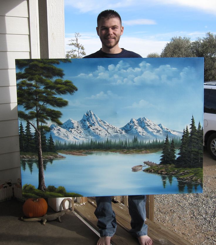 a man holding up a painting in front of a house