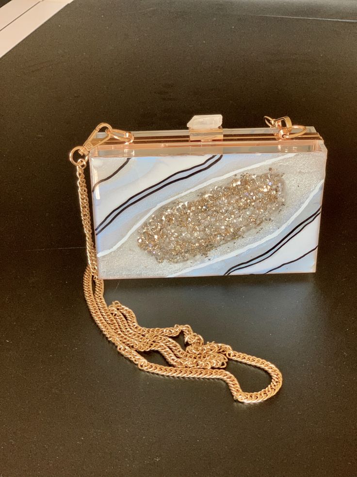 a white and gold purse sitting on top of a black table next to a chain