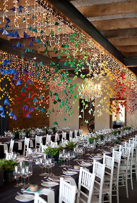 a long table with white chairs and lots of colorful paper butterflies hanging from the ceiling