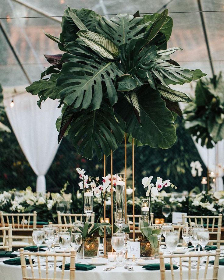 the table is set with white linens, gold chargers and greenery in vases