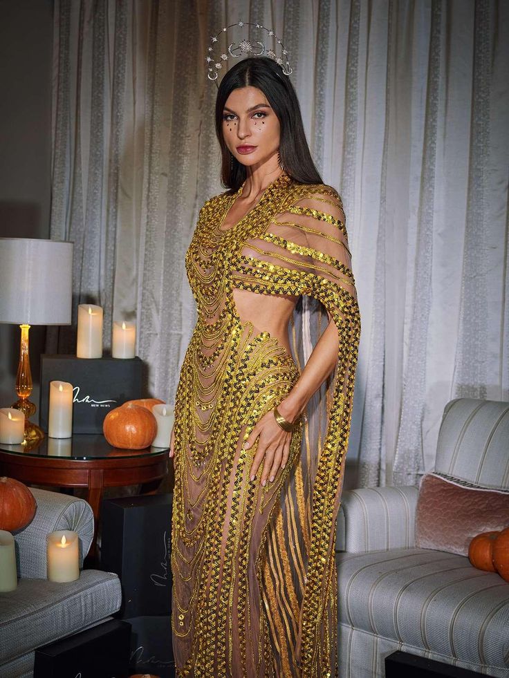 a woman in a gold dress standing next to a couch