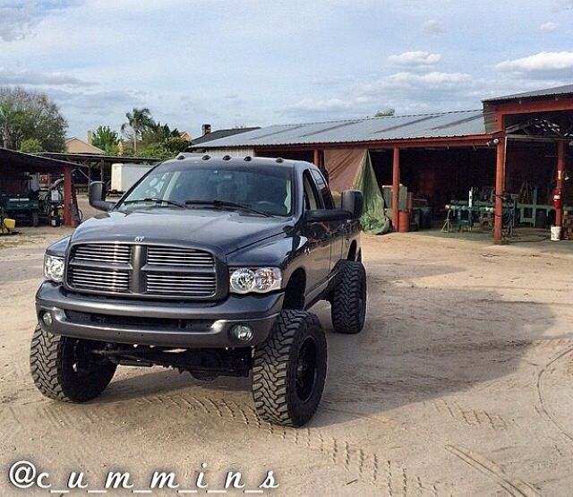 a black dodge ram truck parked in front of a building with large tires on it