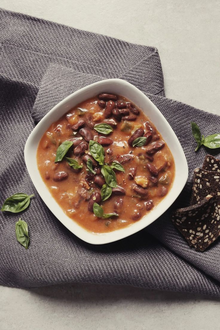 a white bowl filled with beans and spinach on top of a gray napkin next to a black pepper