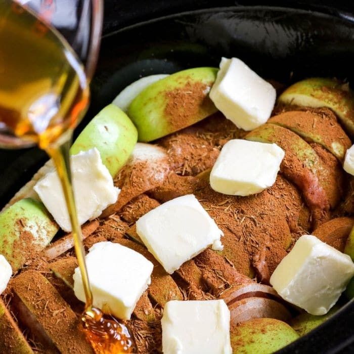 an apple and cheese dish being poured into a slow cooker with butter on top