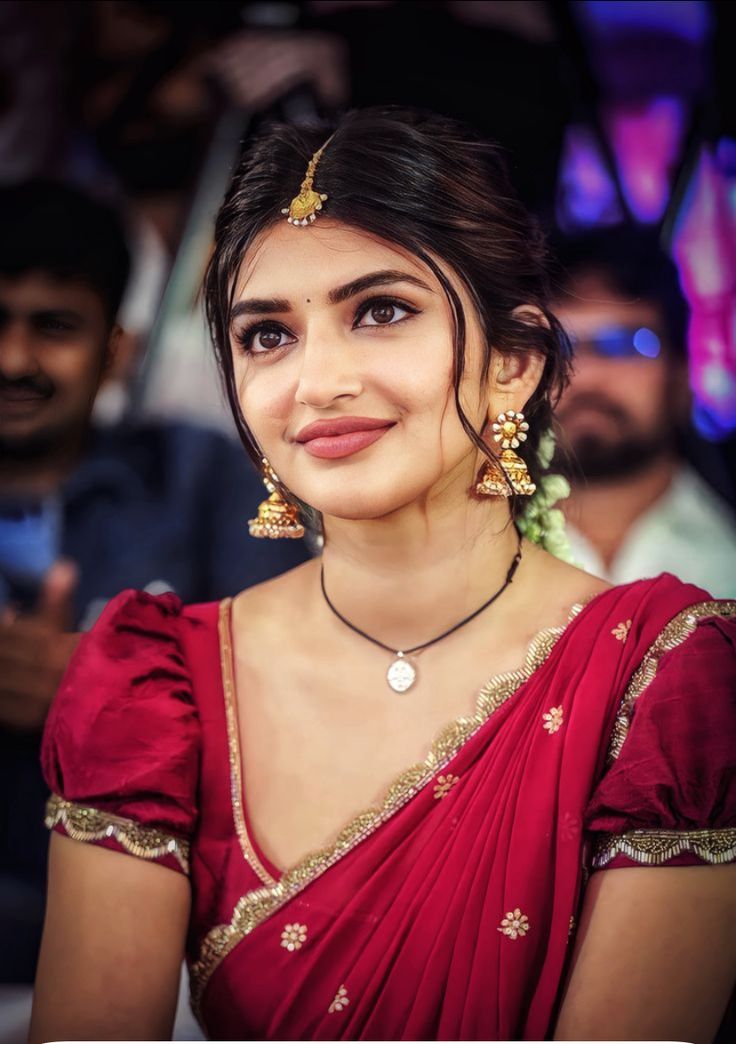 a woman in a red sari with gold jewelry on her neck and shoulders, smiling at the camera