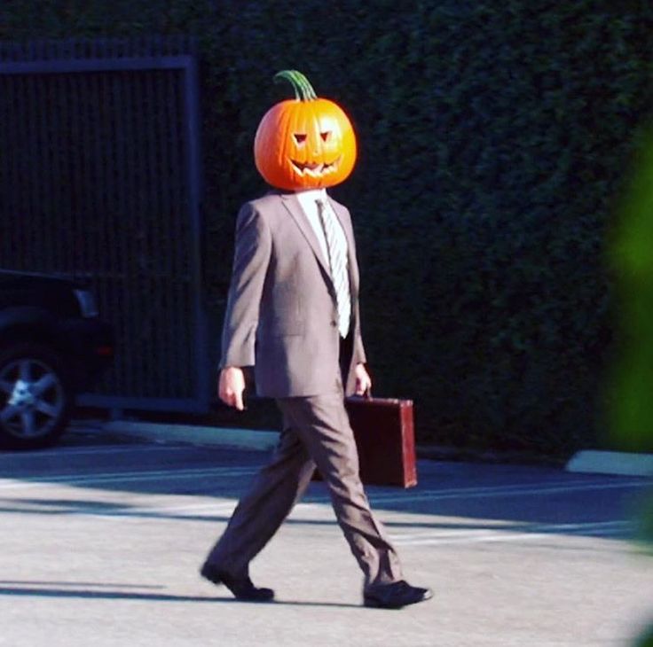 a man in a suit with a pumpkin head on his head walking down the street