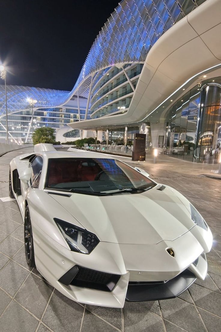 a white sports car parked in front of a large building at night with its lights on