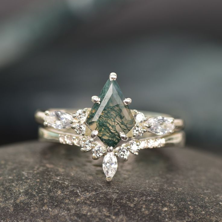 a green and white diamond ring sitting on top of a rock with diamonds around it