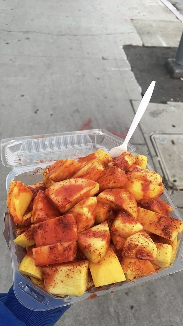 a person holding a plastic container full of food on the sidewalk next to a street