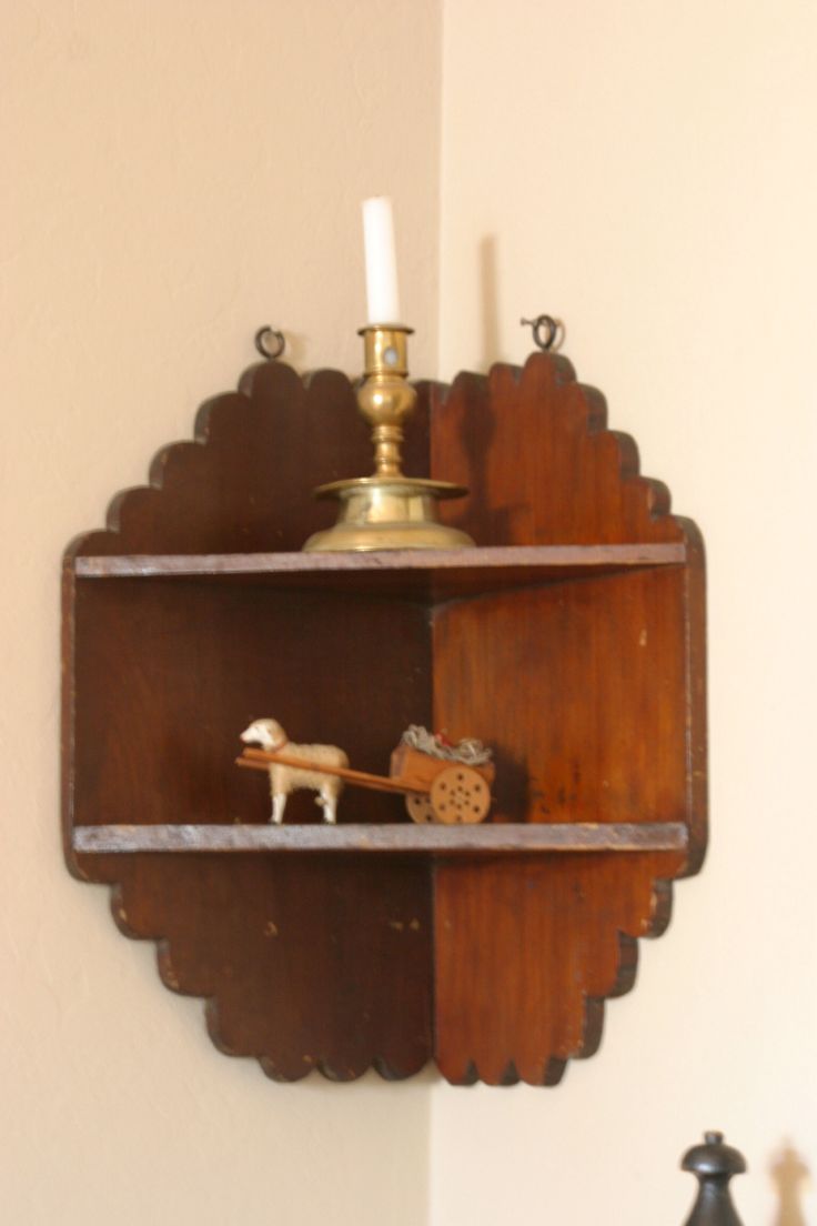 a wooden shelf with a candle and some figurines on it in front of a white wall