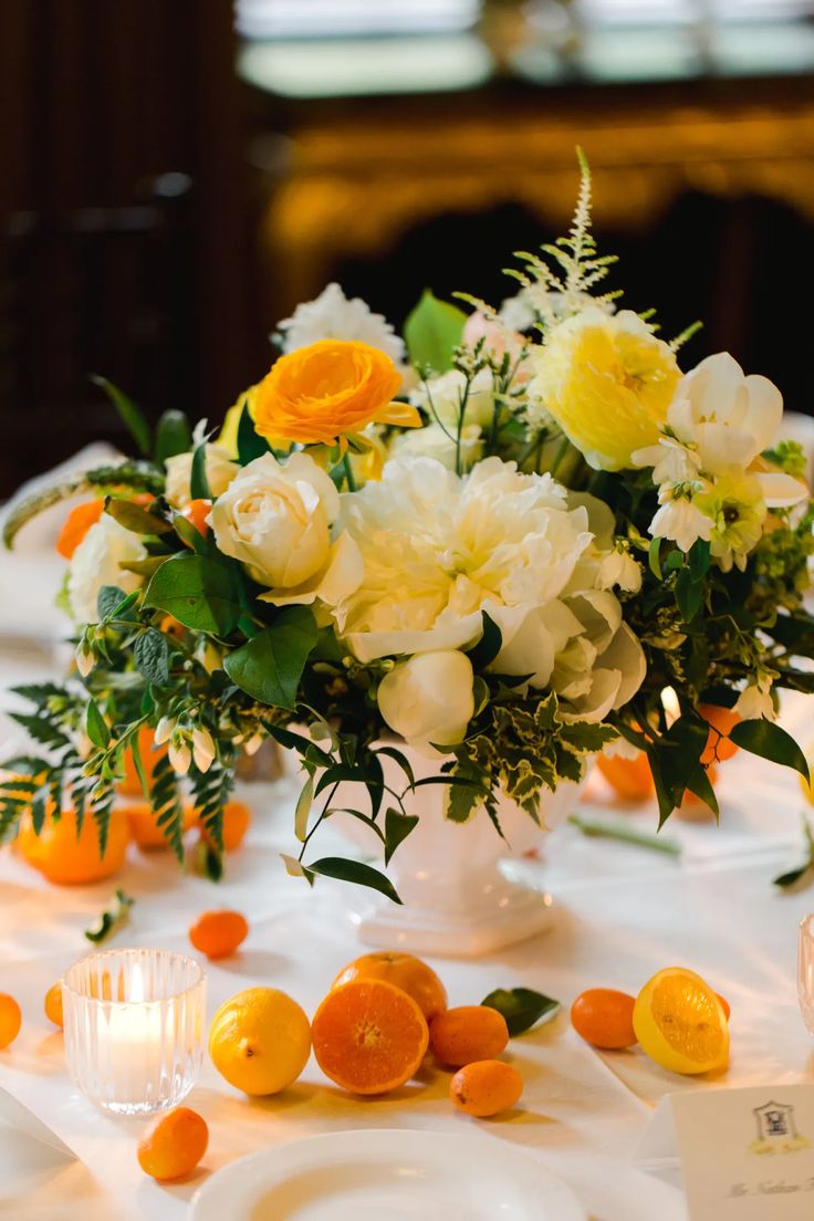 a vase filled with white and yellow flowers on top of a table covered in oranges