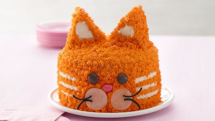 an orange cat cake sitting on top of a white plate next to pink napkins