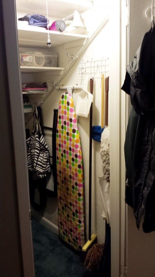 the closet is full of clothes and other items, including an ironing board in it