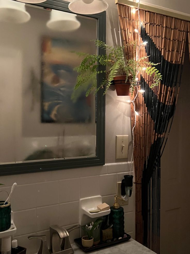 a bathroom sink under a mirror next to a plant and toilet paper dispenser