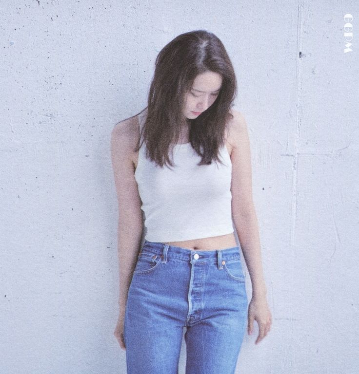 a woman standing in front of a white wall with her hands on her hips and looking down