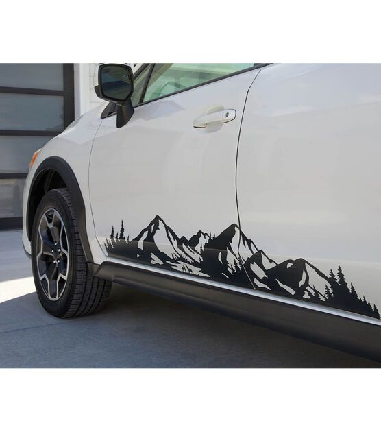 a white car with mountains and trees on it's side, parked in front of a garage door