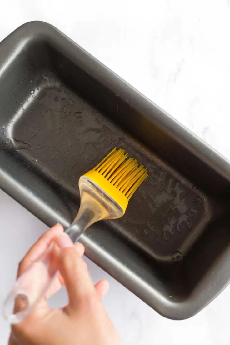 a person is using a brush to clean a pan with something yellow on it that looks like a spatula