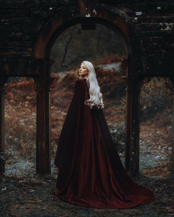 a woman with long white hair wearing a red dress and standing in an old archway