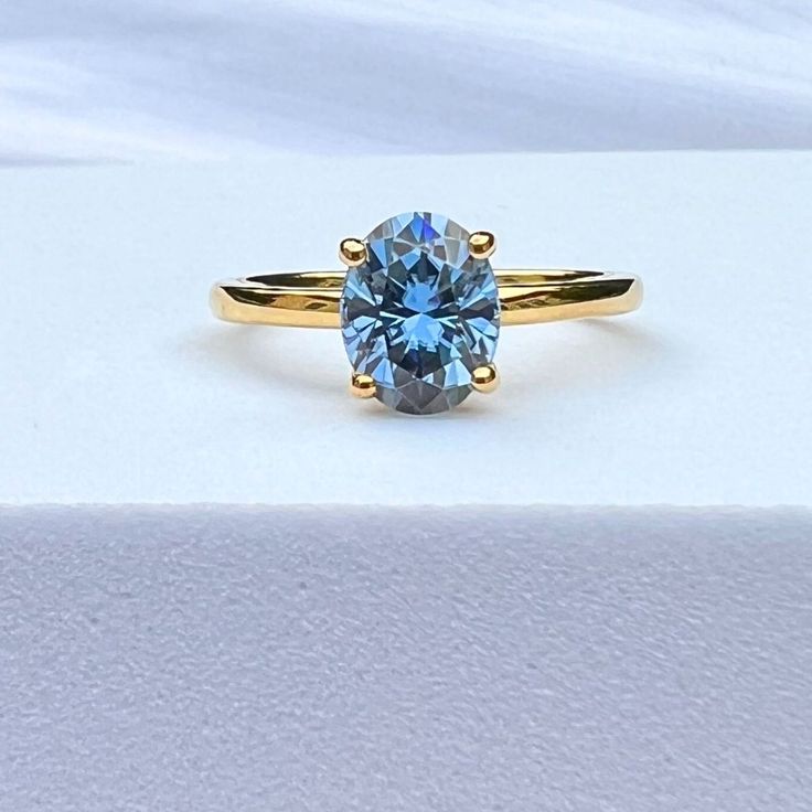 a yellow gold ring with a blue topazte stone in the center, sitting on a white surface