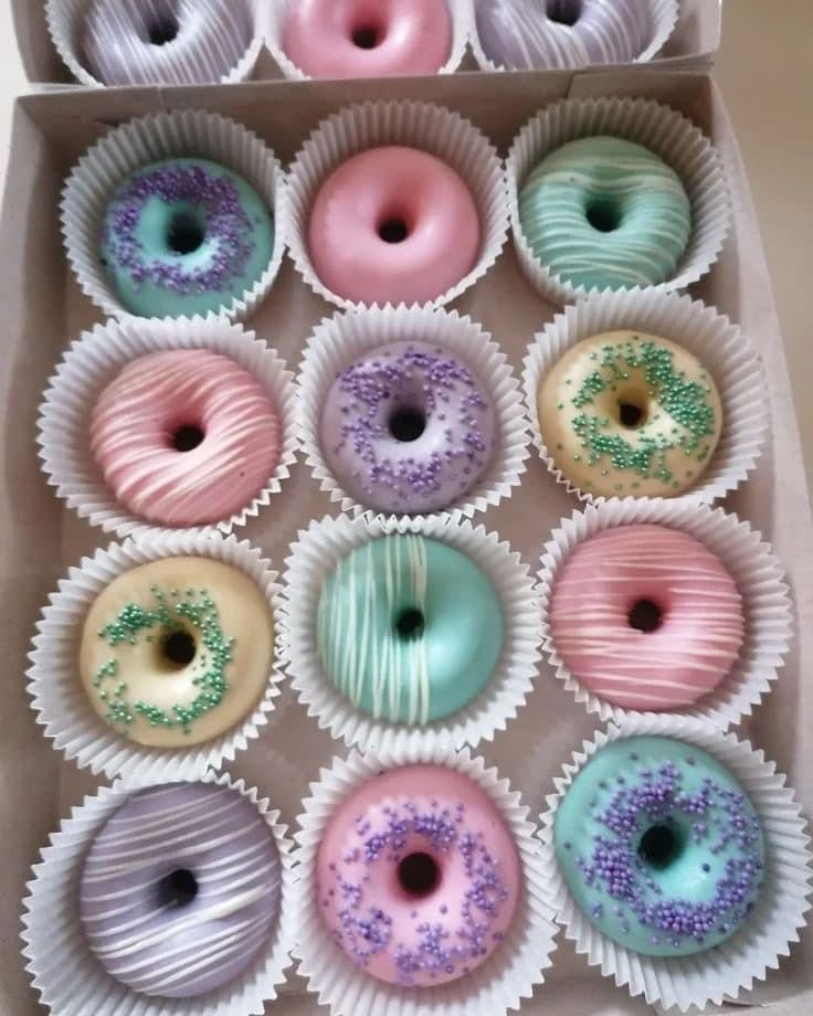 twelve donuts with different colors and designs in a box on the table, ready to be eaten