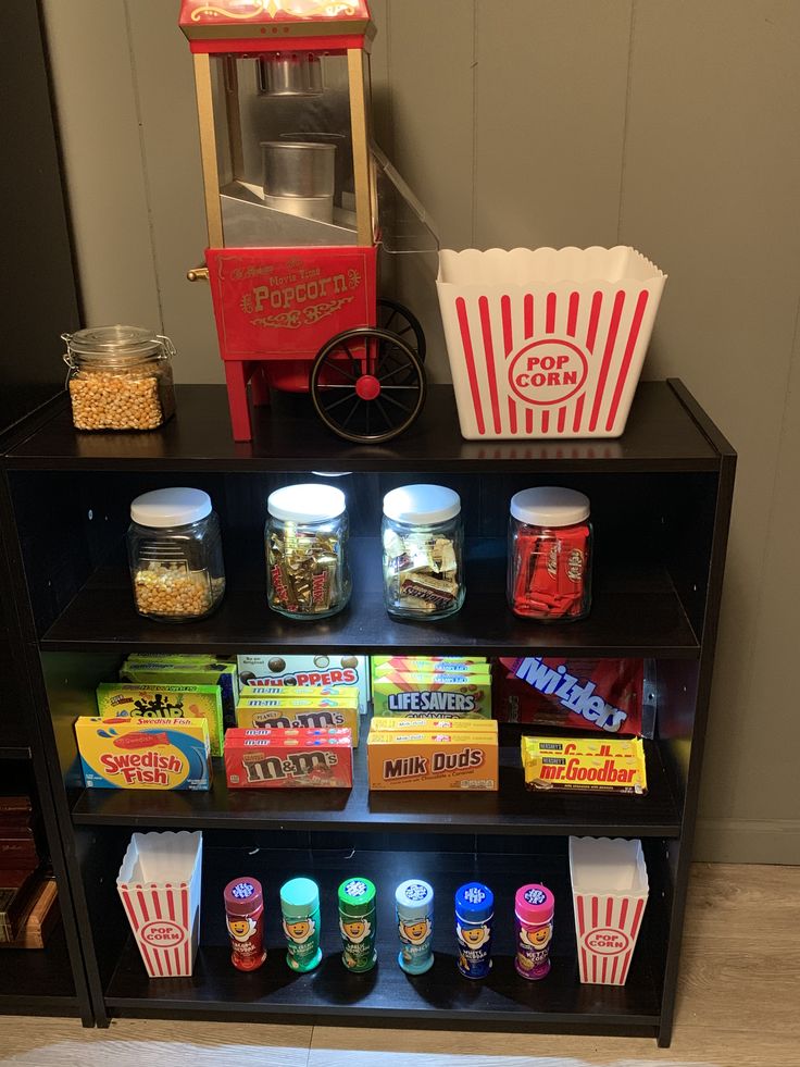 an assortment of snacks and popcorn on a shelf in front of a popcorn machine,