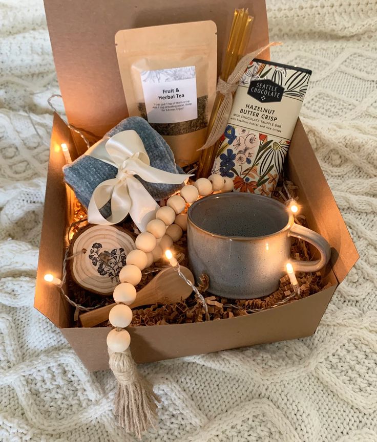 an open box with candles, tea and other items in it on a white blanket