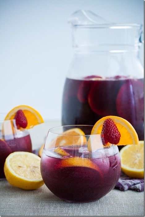 two glasses filled with red liquid and sliced lemons on a table next to a pitcher