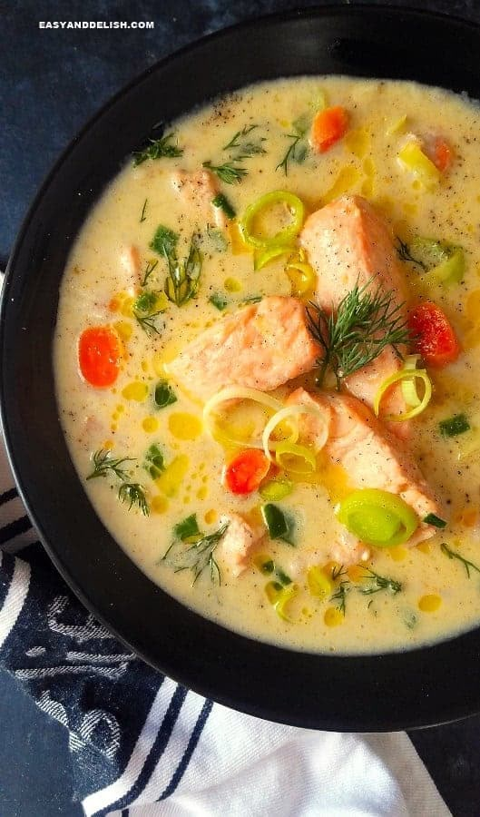 a bowl of soup with salmon and vegetables in it on a blue table cloth next to a white towel