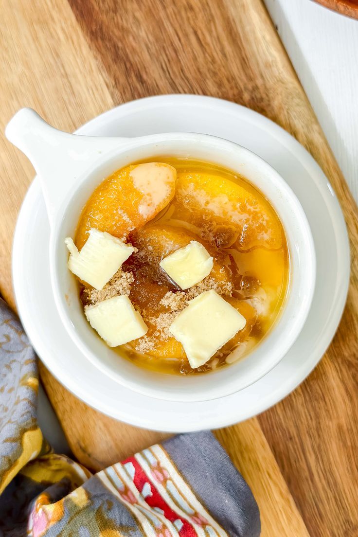 a white bowl filled with fruit and cheese on top of a wooden cutting board next to bread