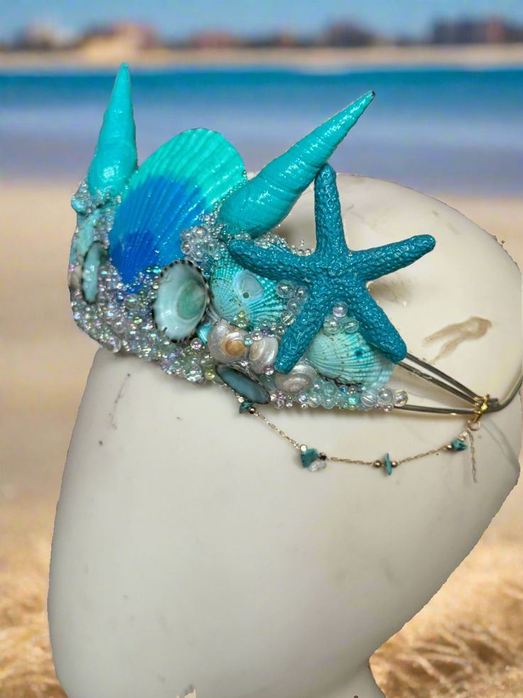 Shimmery Shells Bluesy Mermaid Crown by The Head Mistress Hand-painted shells: Each shell is meticulously hand-painted to capture the beauty of the ocean. Sparkling glitter: Add a touch of sparkle and magic to your mermaid look. Bubble beads: Delicate bubble beads adorn the crown, resembling underwater treasures. Natural moonstone chains: The crown is embellished with natural moonstone chains for an ethereal touch. Available in bold and pastel color palettes: Choose your favorite color palette t Mermaid Look, Bubble Beads, Fantasy Crown, Watercolor Mermaid, Mermaid Crown, Fabric Photography, Simple Skincare Routine, Painted Shells, Sea Witch