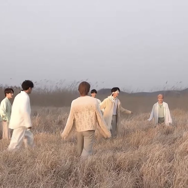 group of people walking through tall grass in open field with one person holding his hand out