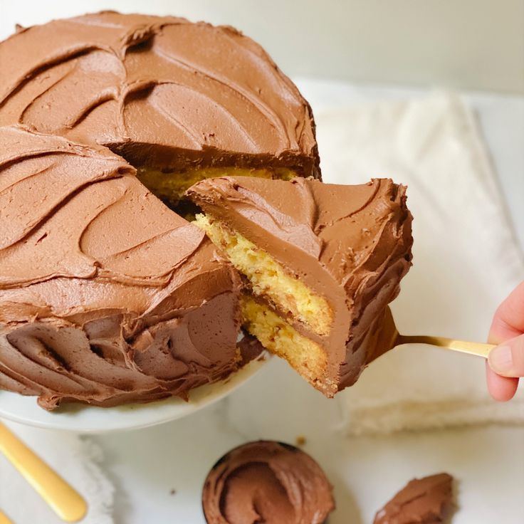 someone is holding a piece of cake with chocolate frosting on it and the rest of the cake has been cut in half