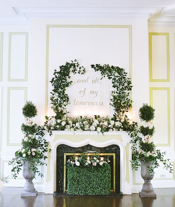 the fireplace is decorated with greenery and white flowers in vases on either side