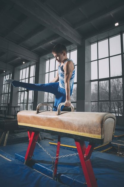 a man standing on top of a bench in front of large windows, with one leg up