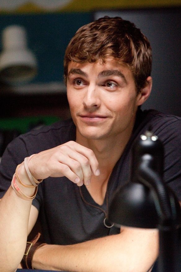 a young man sitting at a table with a wine bottle in front of him and looking to the side