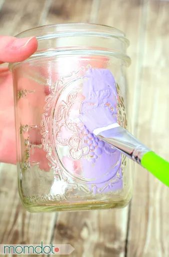 a person is holding a mason jar with purple paint and a green toothbrush in it