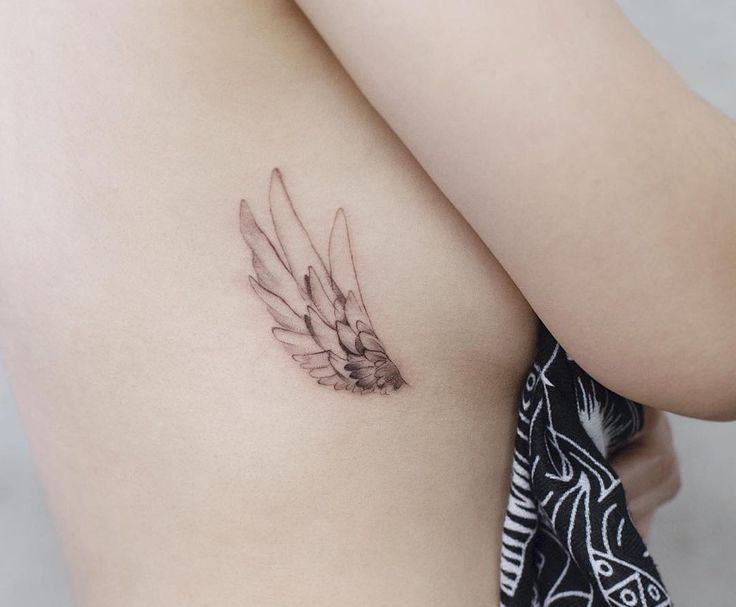 a small tattoo on the back of a woman's left shoulder, with feathers