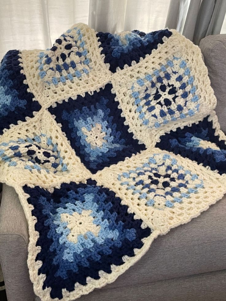 a blue and white crocheted blanket sitting on top of a couch next to a window