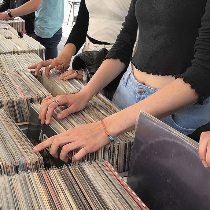 several people standing at a long table with records on it and holding their hands together